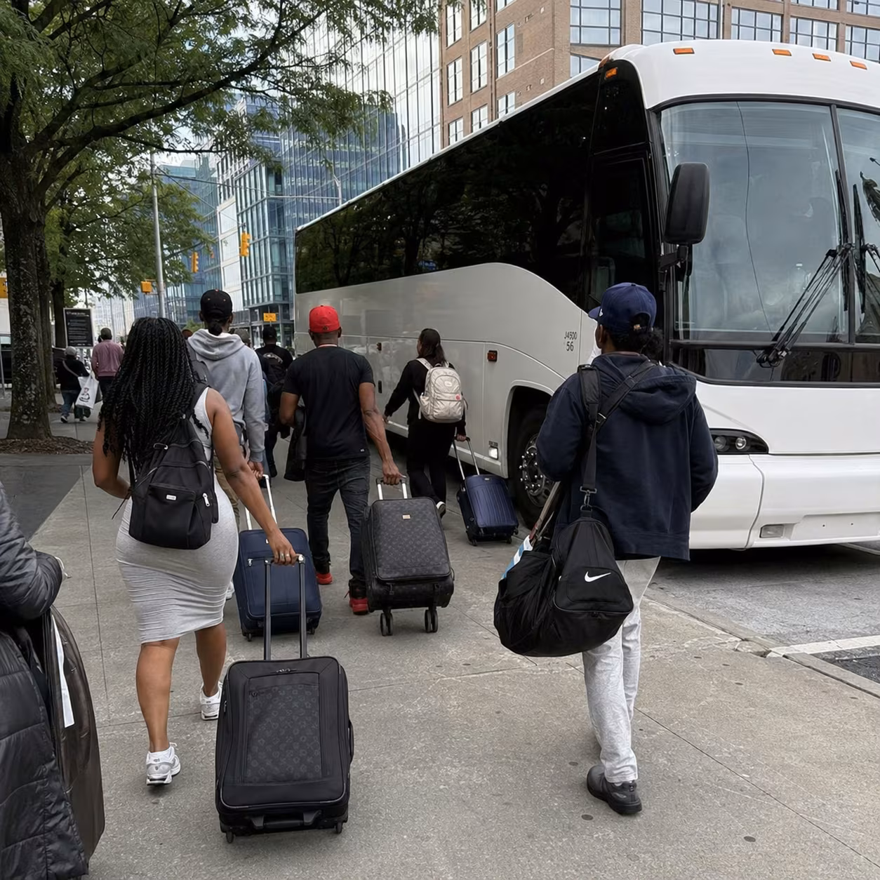Corporate group with rolling luggage boarding a white charter bus